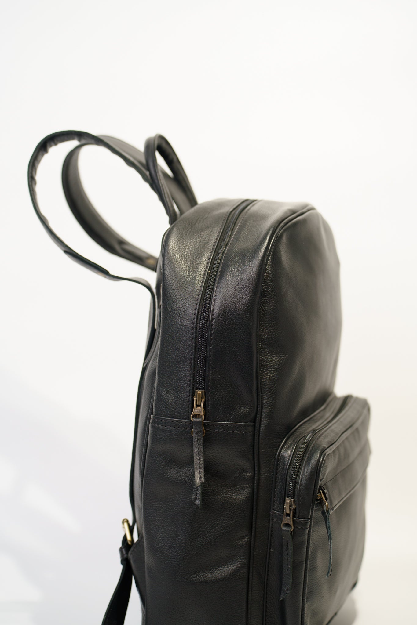 Close side view of Chamra's black leather bag with a hand carry strap, shoulder straps, and side pockets for maximum utility.