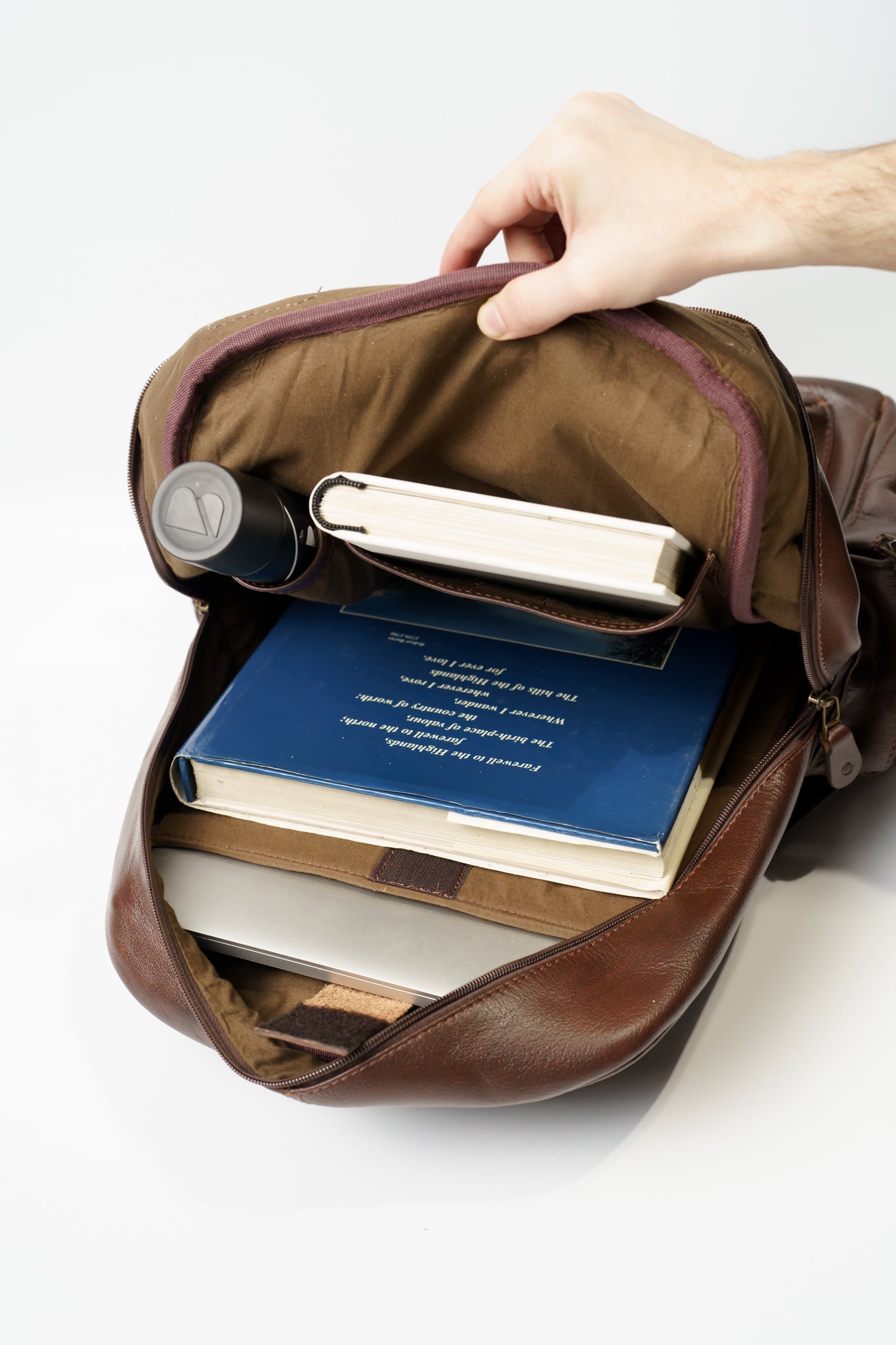Inner view of Chamra's brown leather backpack showcasing compartments for laptops, notebooks, and water bottles.