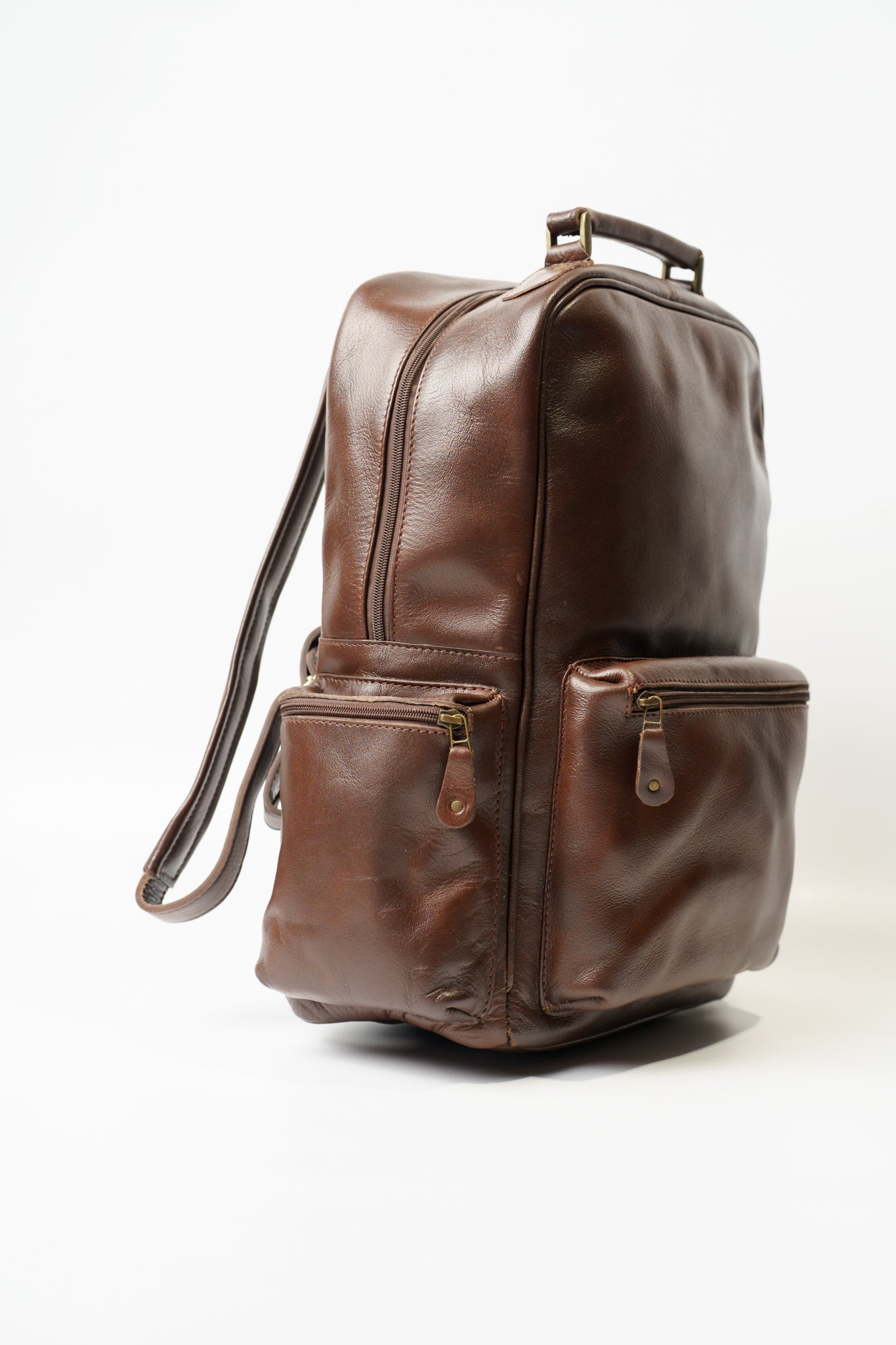 Side view of Chamra's brown leather backpack showcasing three distinct pockets, two on the sides and one on the front, each with zipper closure.