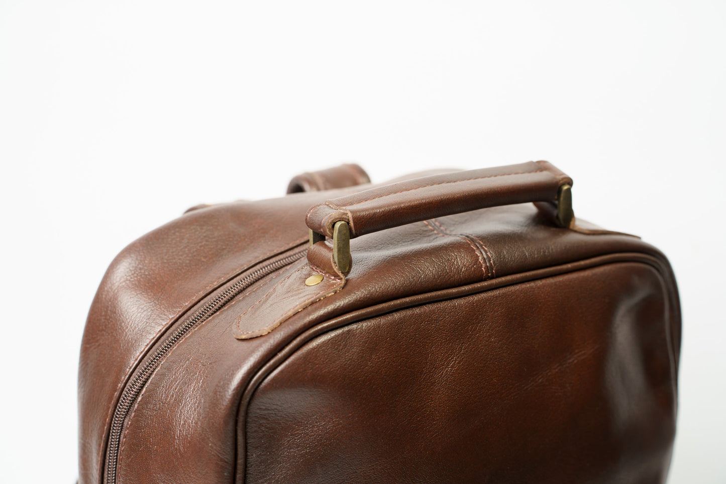 Close-up of the hand carry strap on Chamra's brown leather backpack.