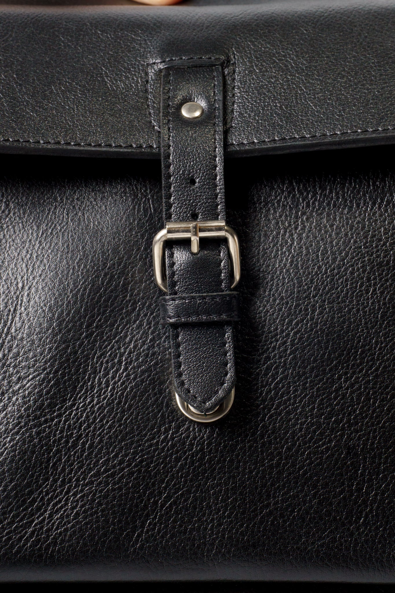 Close up of the front clasp buckle closure on Chamra's laptop bag. The imag showcases the superior stitching quality and metallic finish.